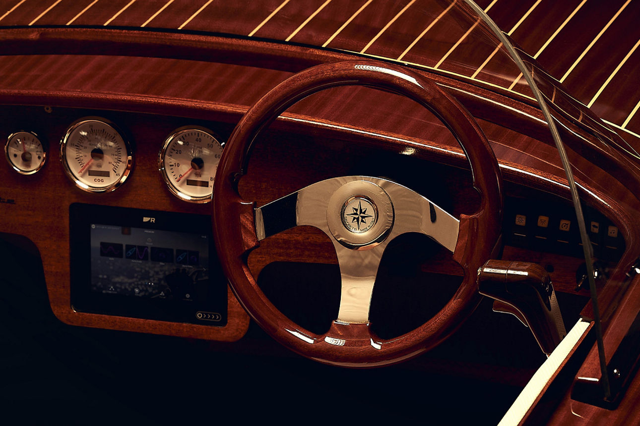 Nahaufnahme eines klassischen Cockpits mit Holzlenkrad, analogen Anzeigen und polierter Holzarmatur.