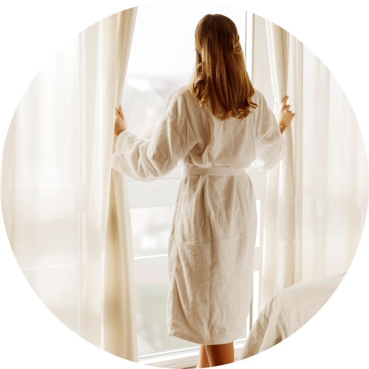 Frau im Bademantel steht vor einem Fenster