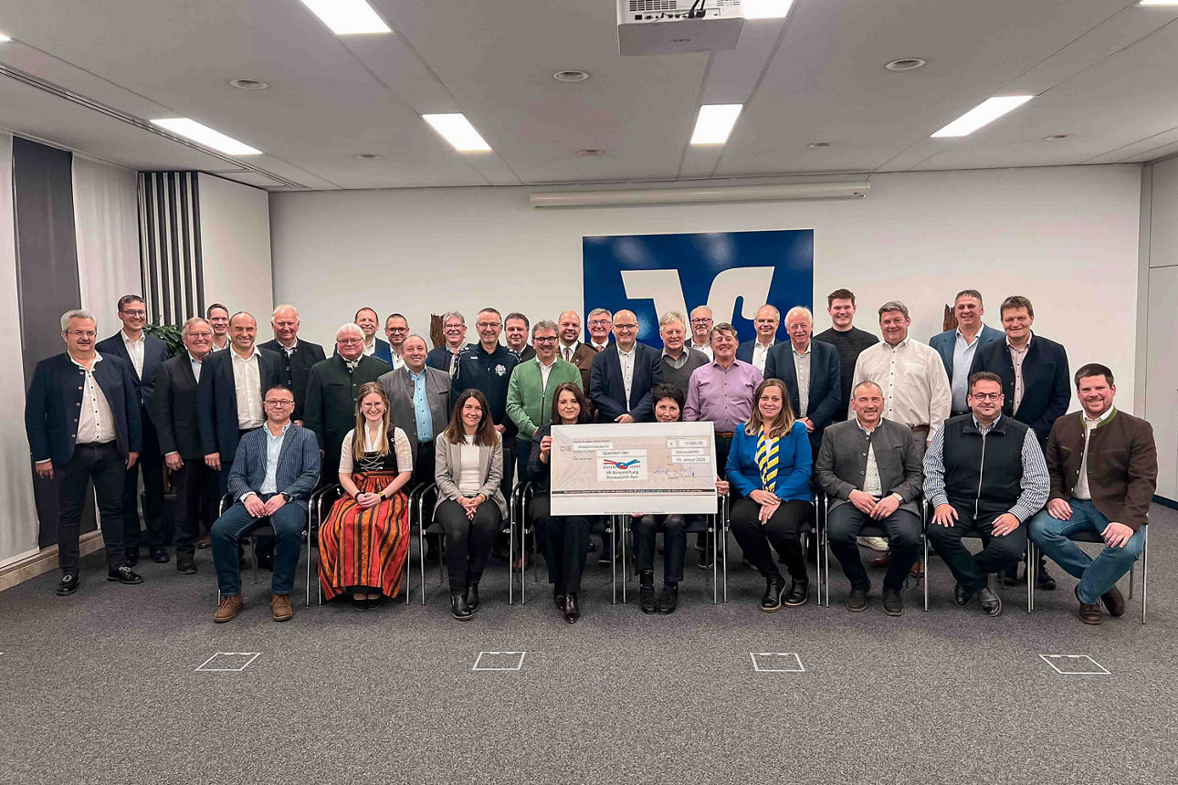 Große Gruppe von Erwachsenen posiert gemeinsam mit einem symbolischen Schlüssel vor einem Firmenlogo.