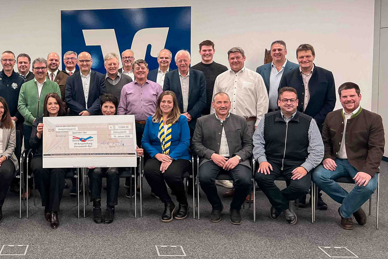 Große Gruppe von Erwachsenen posiert gemeinsam mit einem symbolischen Schlüssel vor einem Firmenlogo.