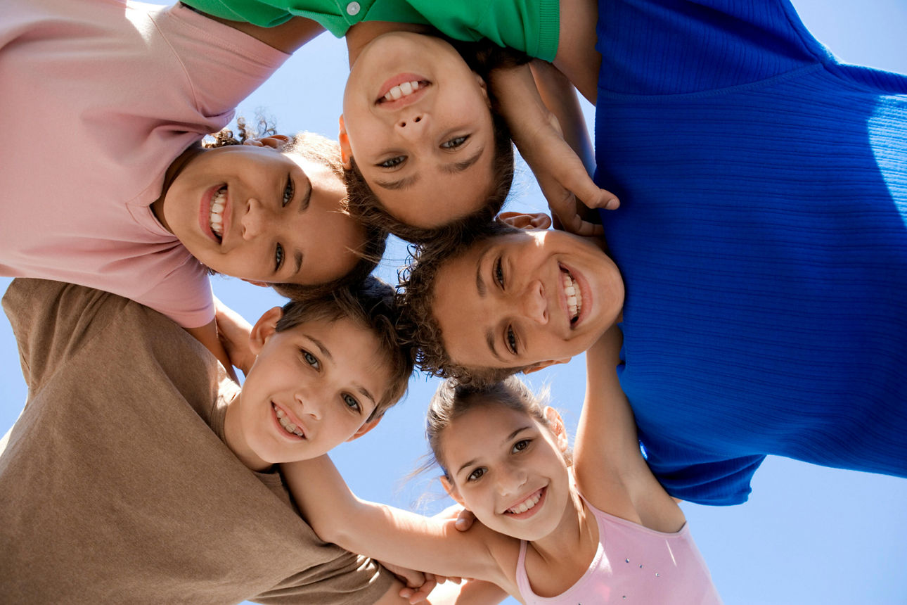 Eine Gruppe von Kindern steht Arm in Arm im Kreis und lächelt in die Kamera.