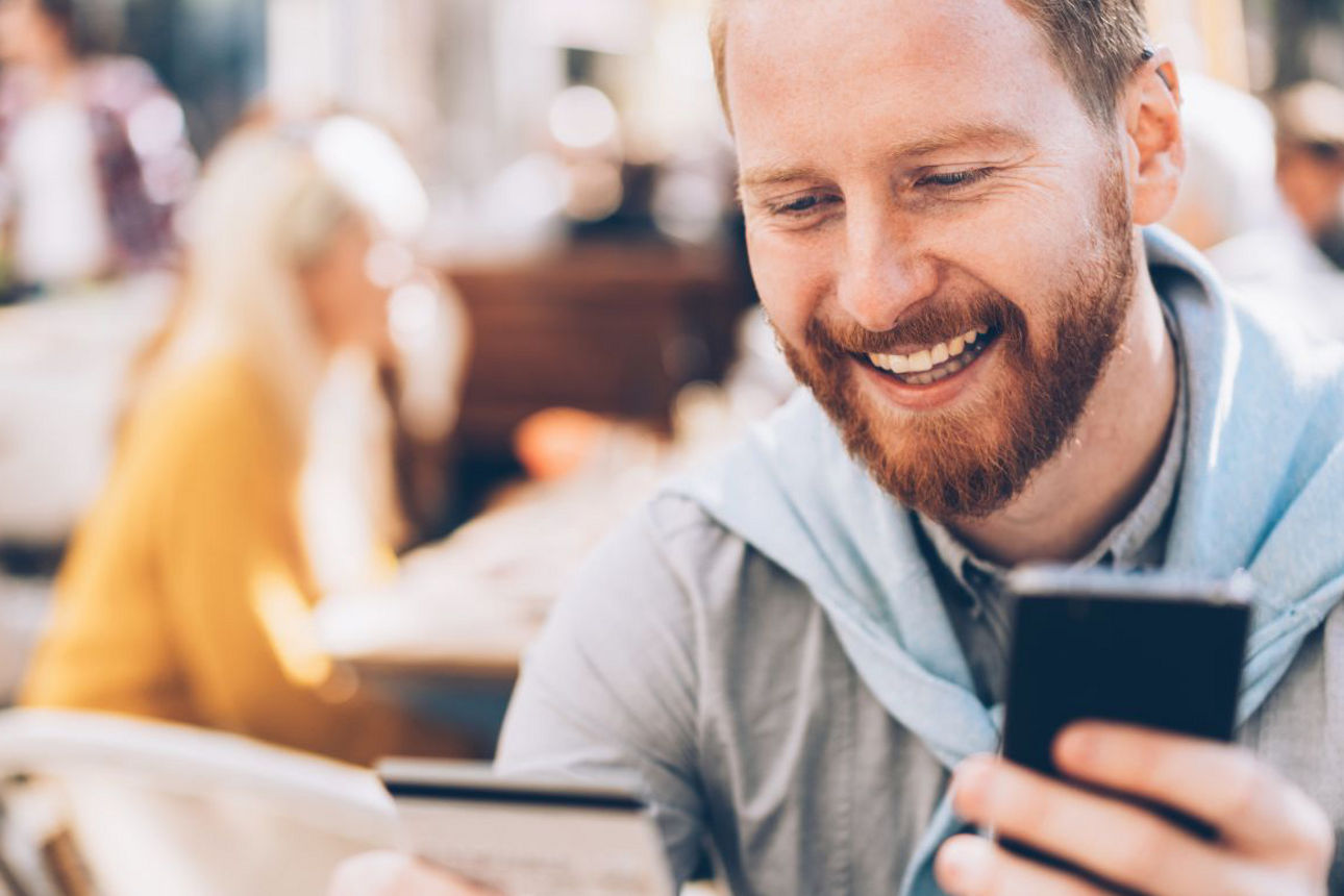 Person sitzt in einem Café oder Außenbereich, hält ein Smartphone in der einen Hand und eine Bankkarte in der anderen.