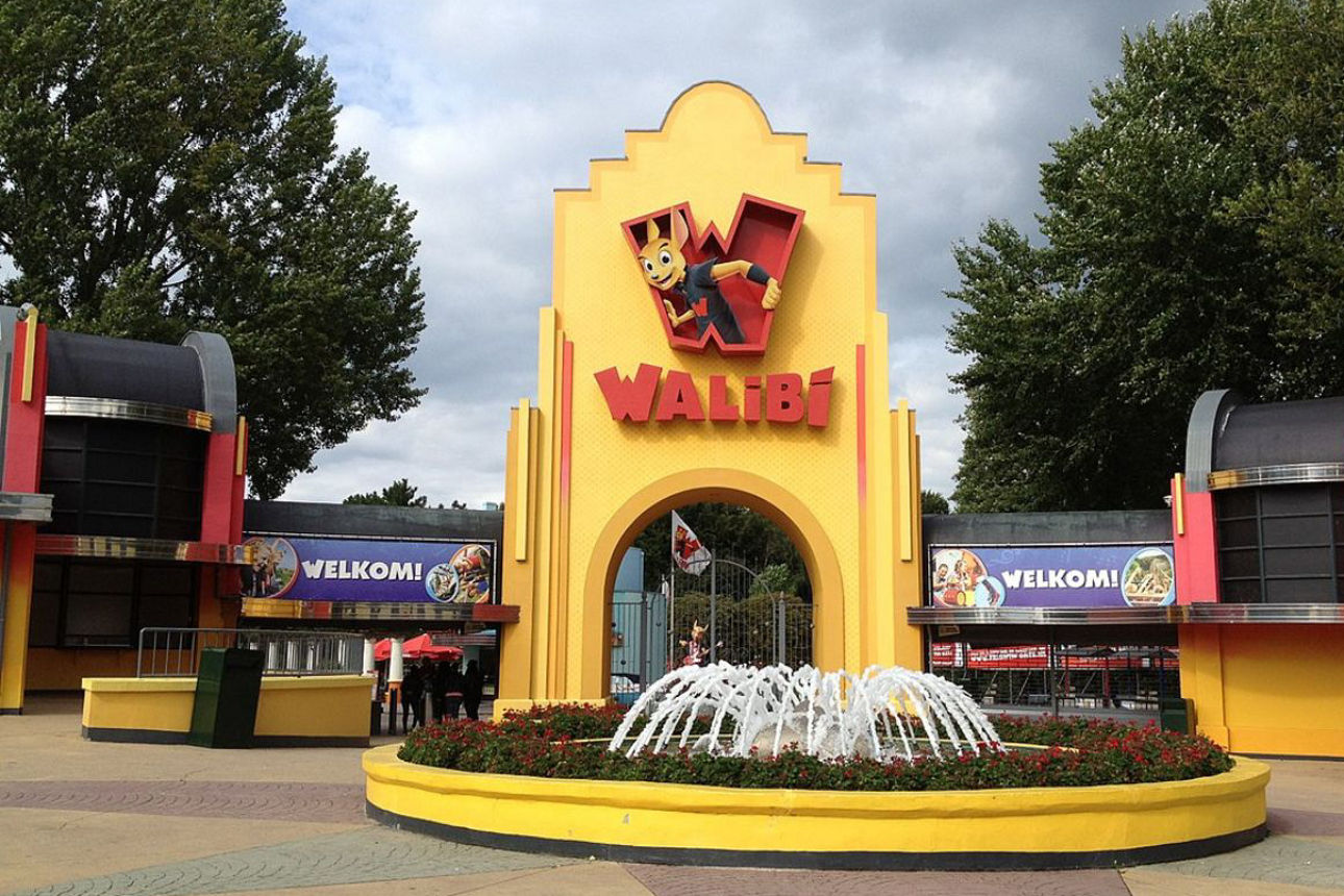 Gelber Eingangsbereich des Freizeitparks Walibi mit rotem Schriftzug und Comic-Känguru über dem Tor, umgeben von grünen Bäumen.