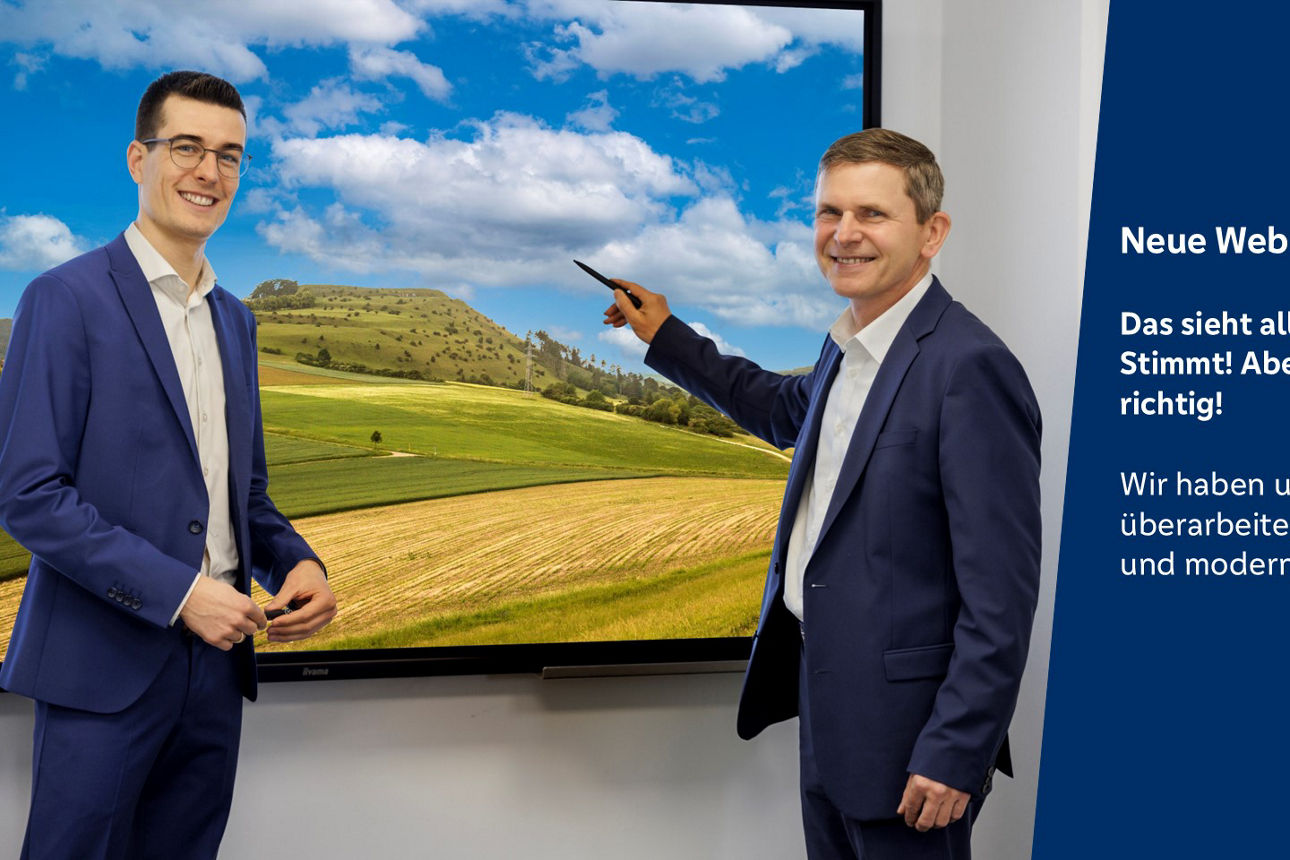 Zwei Männer stehen vor einem Bildschirm mit einem werblichen Text zu einem neuen Internetauftritt.