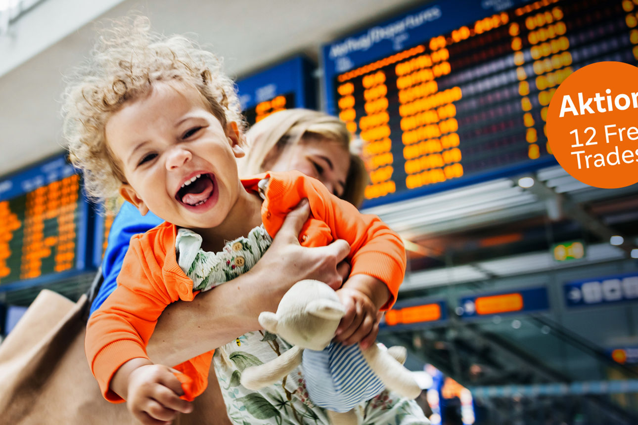 Junge Frau hält ihr lachendes Kind in den Armen, im Hintergrund eine Abflugtafel am Flughafen