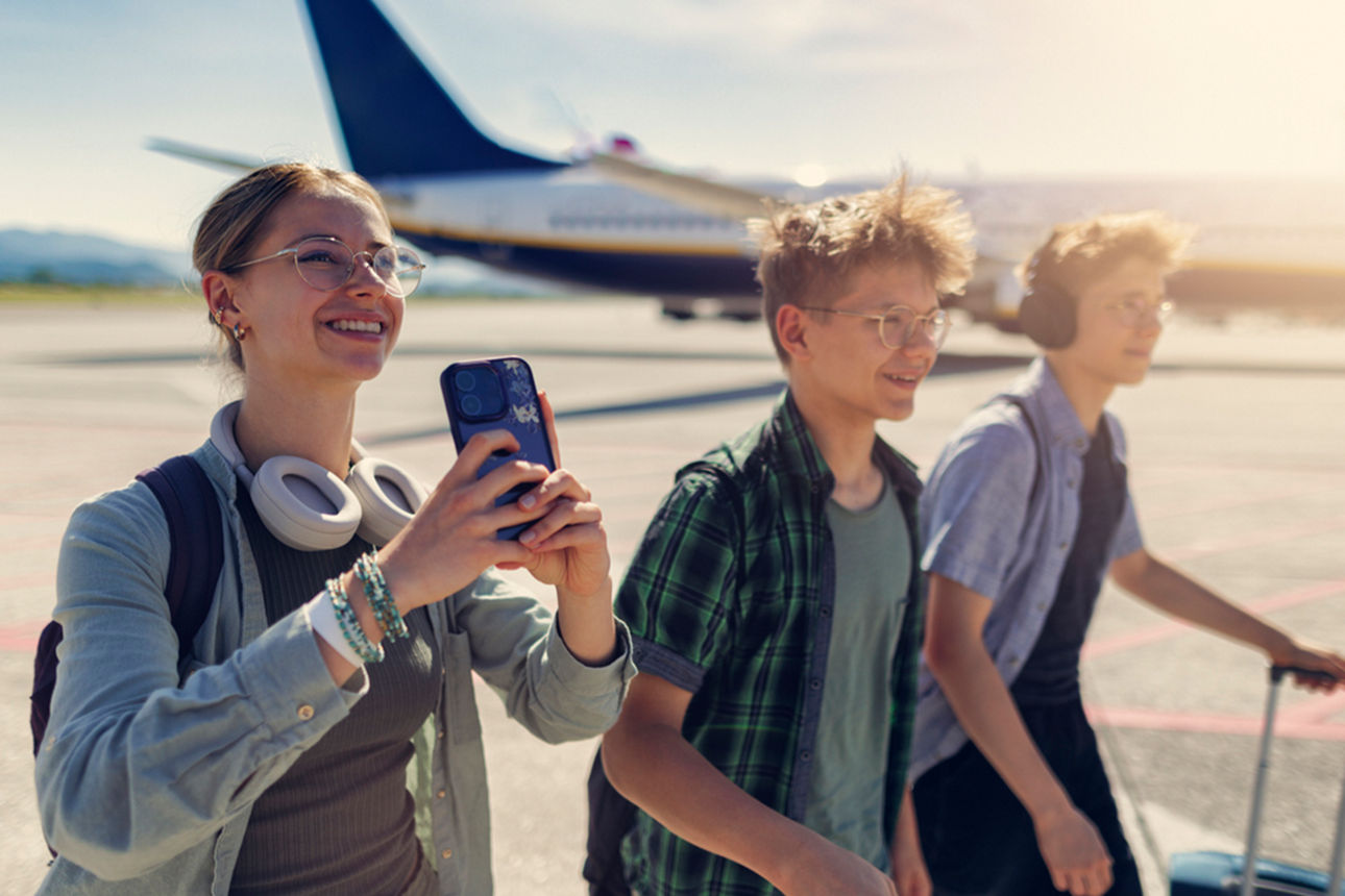Drei Teenager laufen glücklich übers Rollfeld. Eine hat ihr Handy in der Hand.