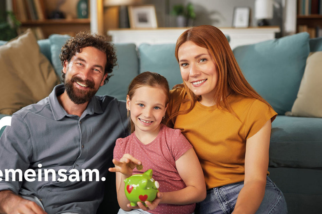 Eine Familie sitzt lächelnd vor einem Sofa, während ein Kind Geld in ein grünes Sparschwein wirft. Links steht der Text „Wir 