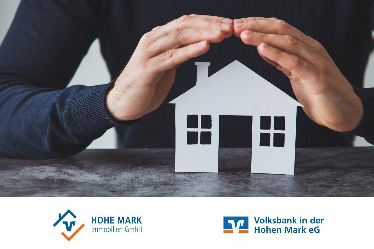 Papiermodell eines Hauses auf einem Tisch, darüber schützend gehaltene Hände. Daneben die Logos von Hohe Mark Immobilien GmbH und Volksbank in der Hohen Mark eG.