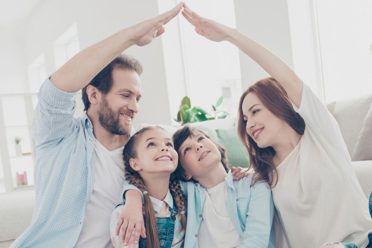 Familie vor weißem Sofa, formt mit Händen ein Dach