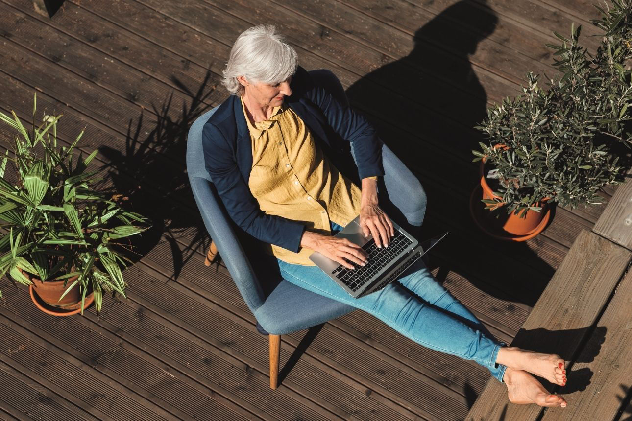 Person arbeitet mit einem Laptop auf einer Terrasse zwischen Topfpflanzen.