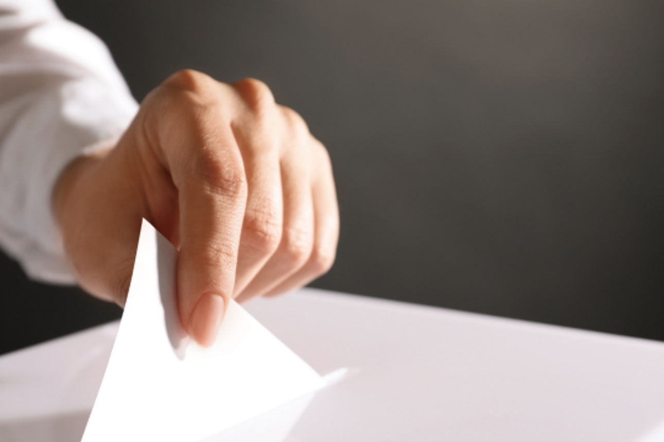 Hand wirft einen Zettel in eine Wahlurne