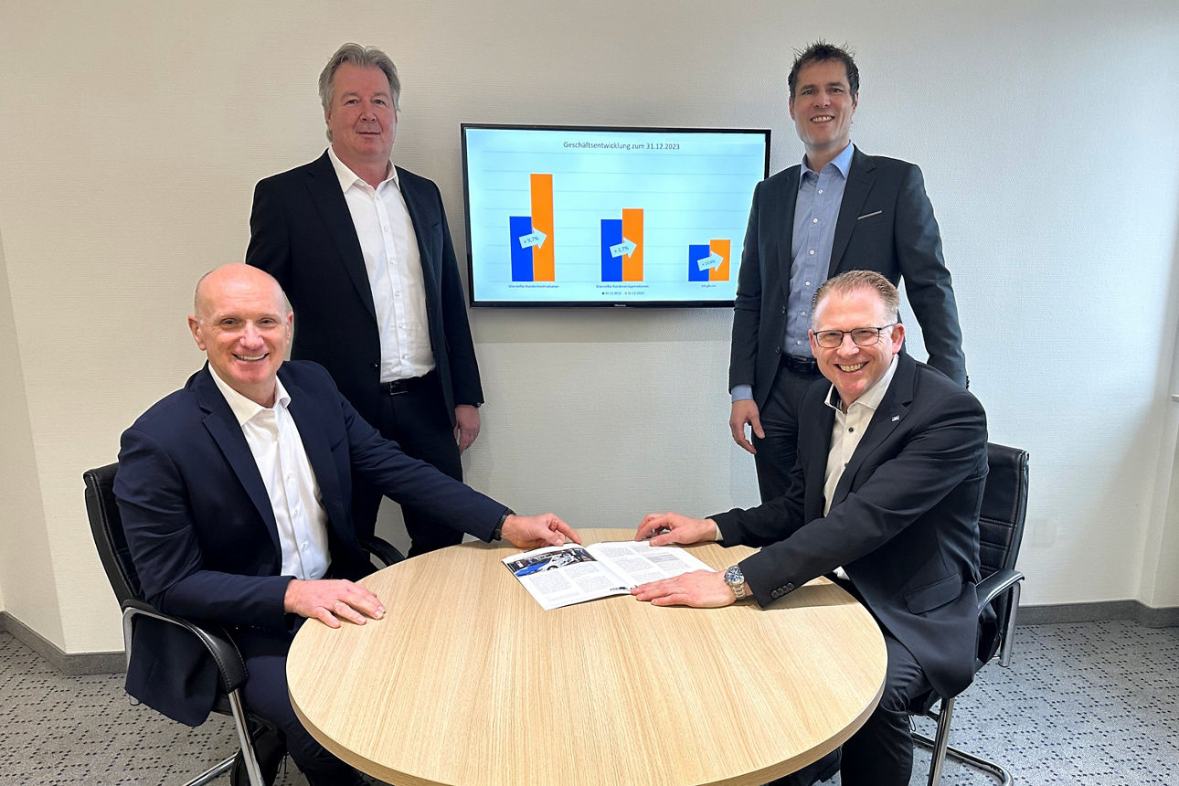 Vier Männer in Geschäftsanzügen stehen vor einem Gebäude