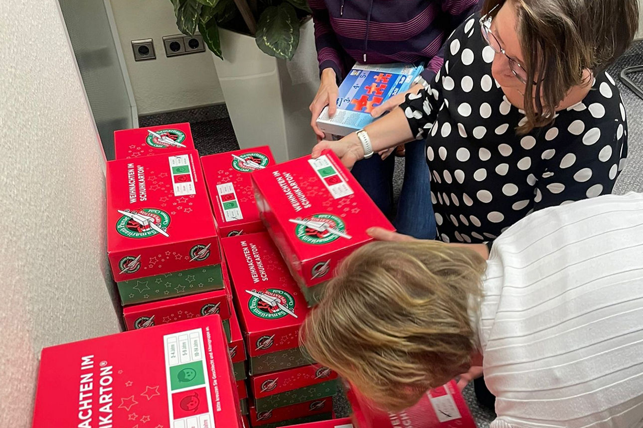 Drei Frauen stapeln gepackte Kartons für "Weihnachten im Schuhkarton".