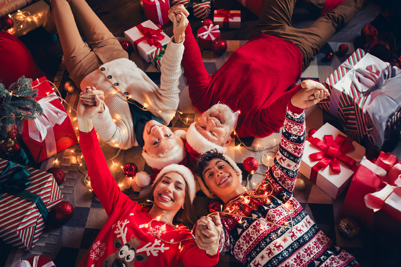Familie in Weihnachtspullis liegt händehaltend am Boden um sie herum liegen Geschenke