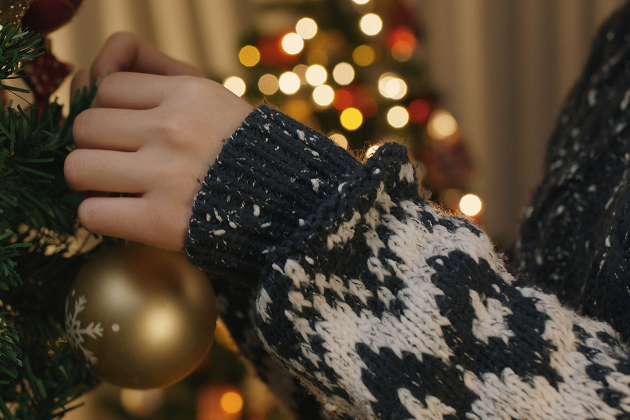 Ein Kind hängt eine goldene Weihnachtskugel an den geschmückten Tannenbaum