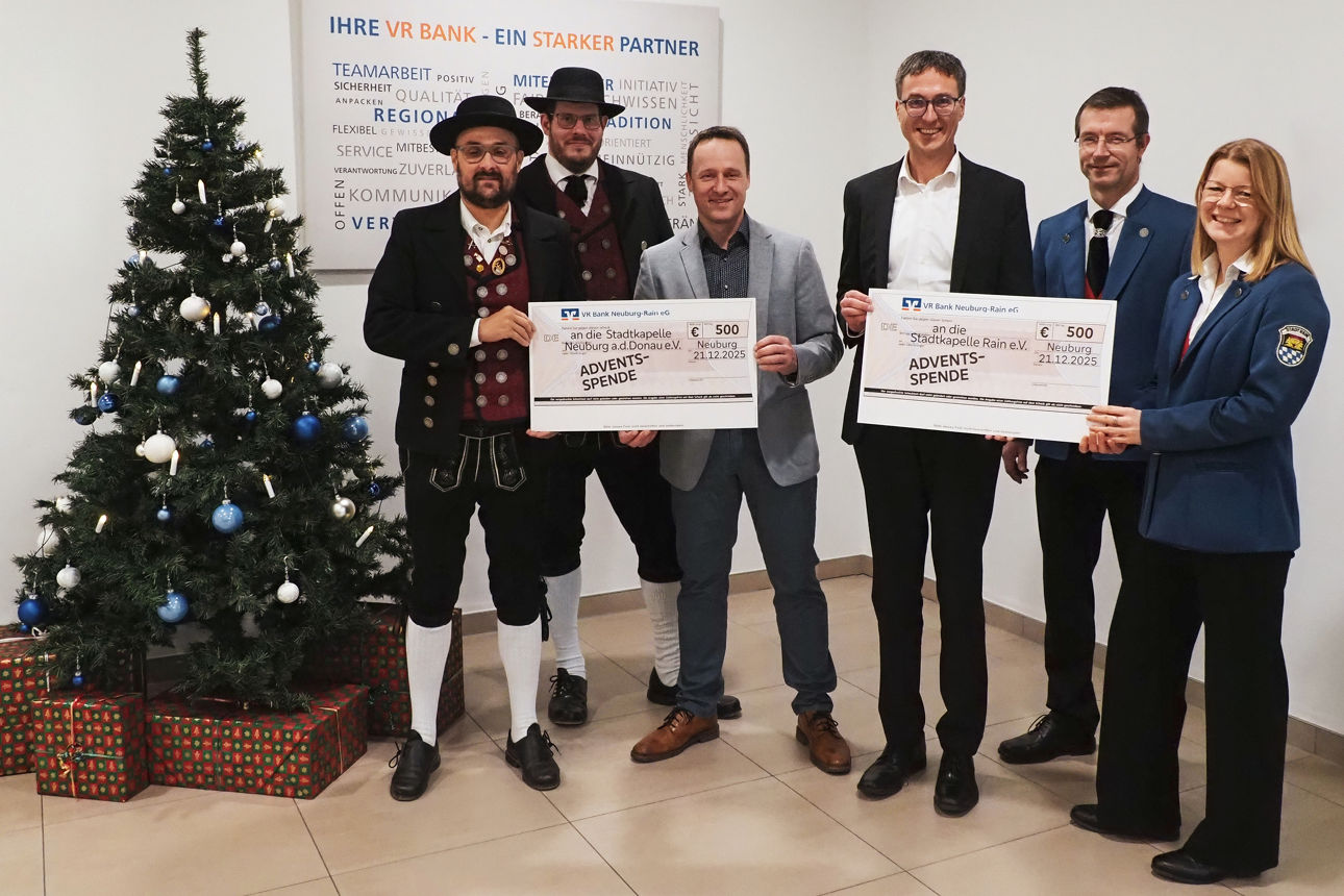 Sechs Personen mit zwei Spendenschecks in der Hand neben einem Christbaum