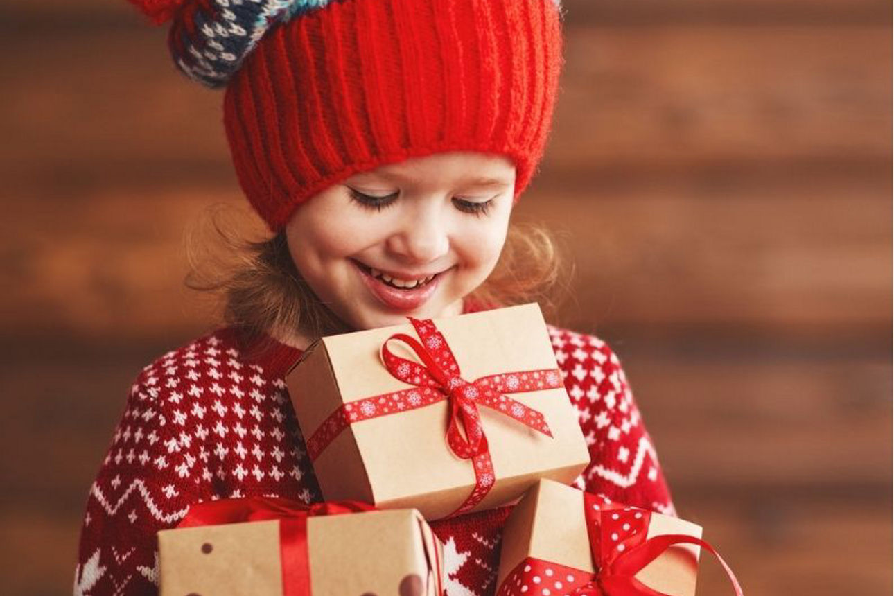 Kind in Weihnachtspulli trägt viele Geschenke