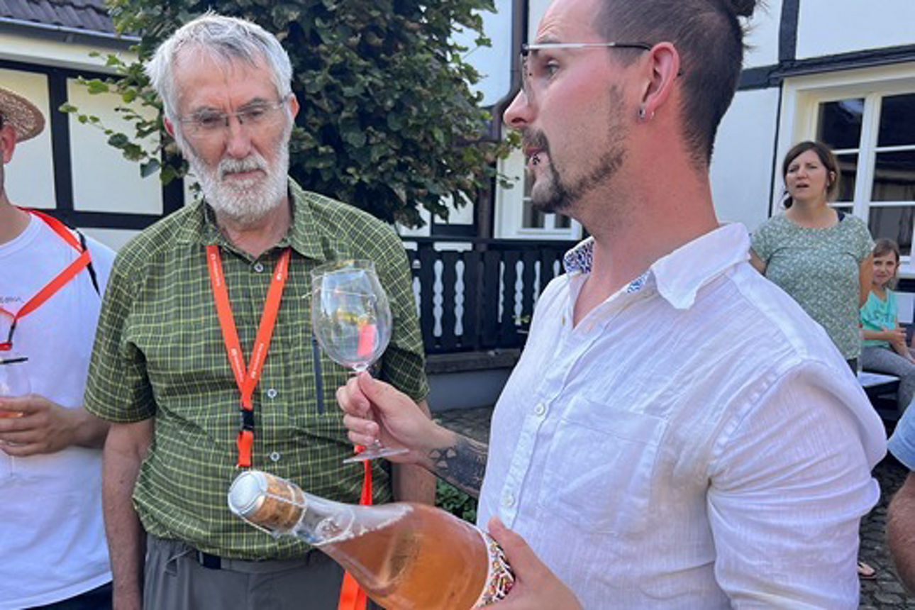 Mehrere Personen, wovon ein Mann ein Weinglas und eine Flasche Wein in der Hand hält