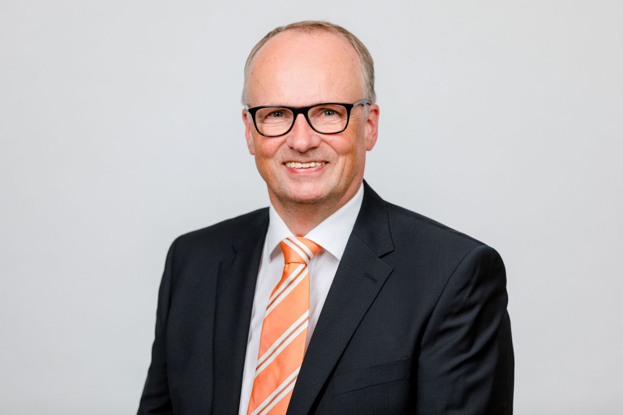 Ein lächelnder Mann in einem Anzug schaut in die Kamera.