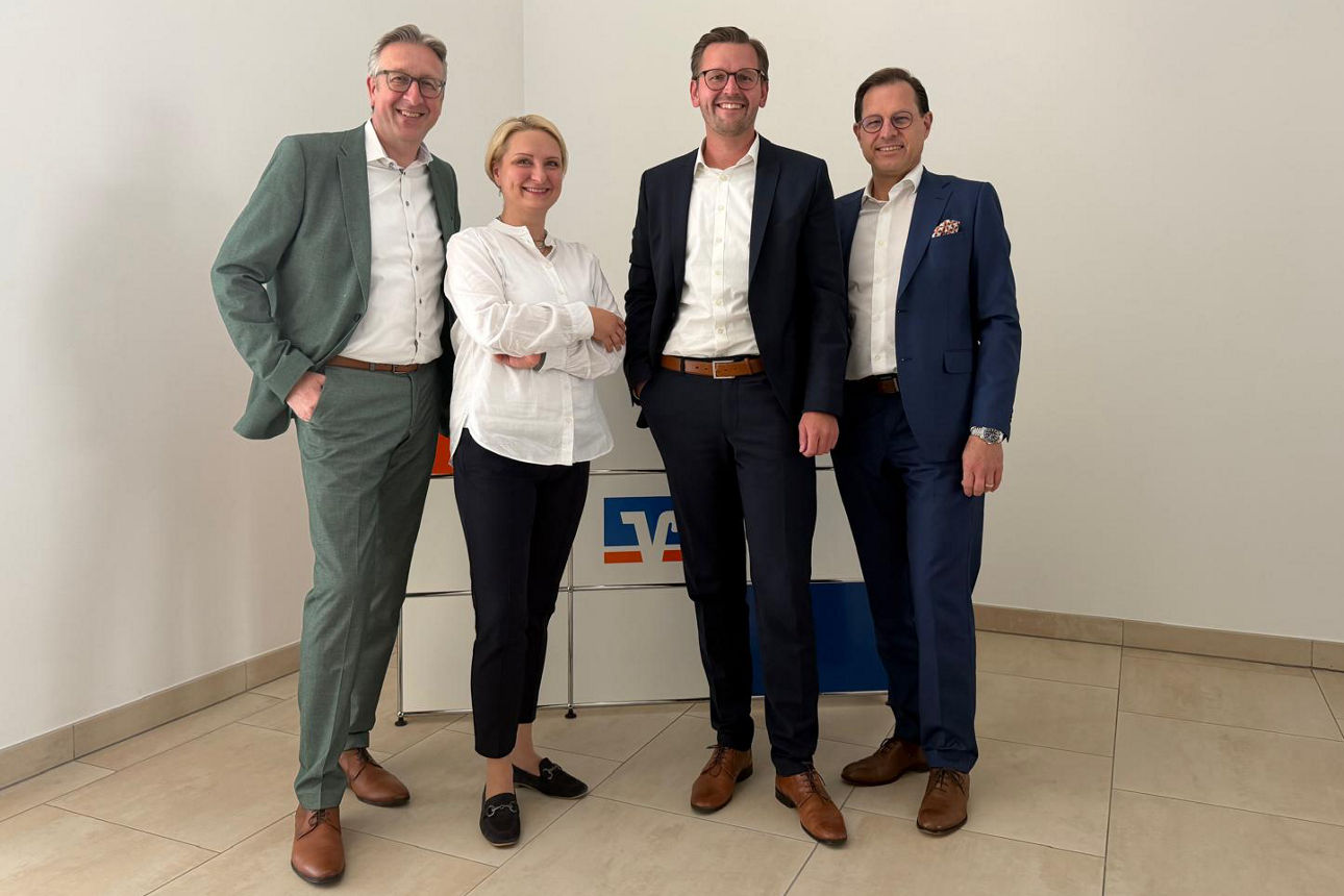 Auf dem Bild stehen der Vorstandsvorsitzende, die Bereichsleiterin Personal und der stellv. Vorstandsvorsitzende der Bank und gratulieren Marcel Reitner. 