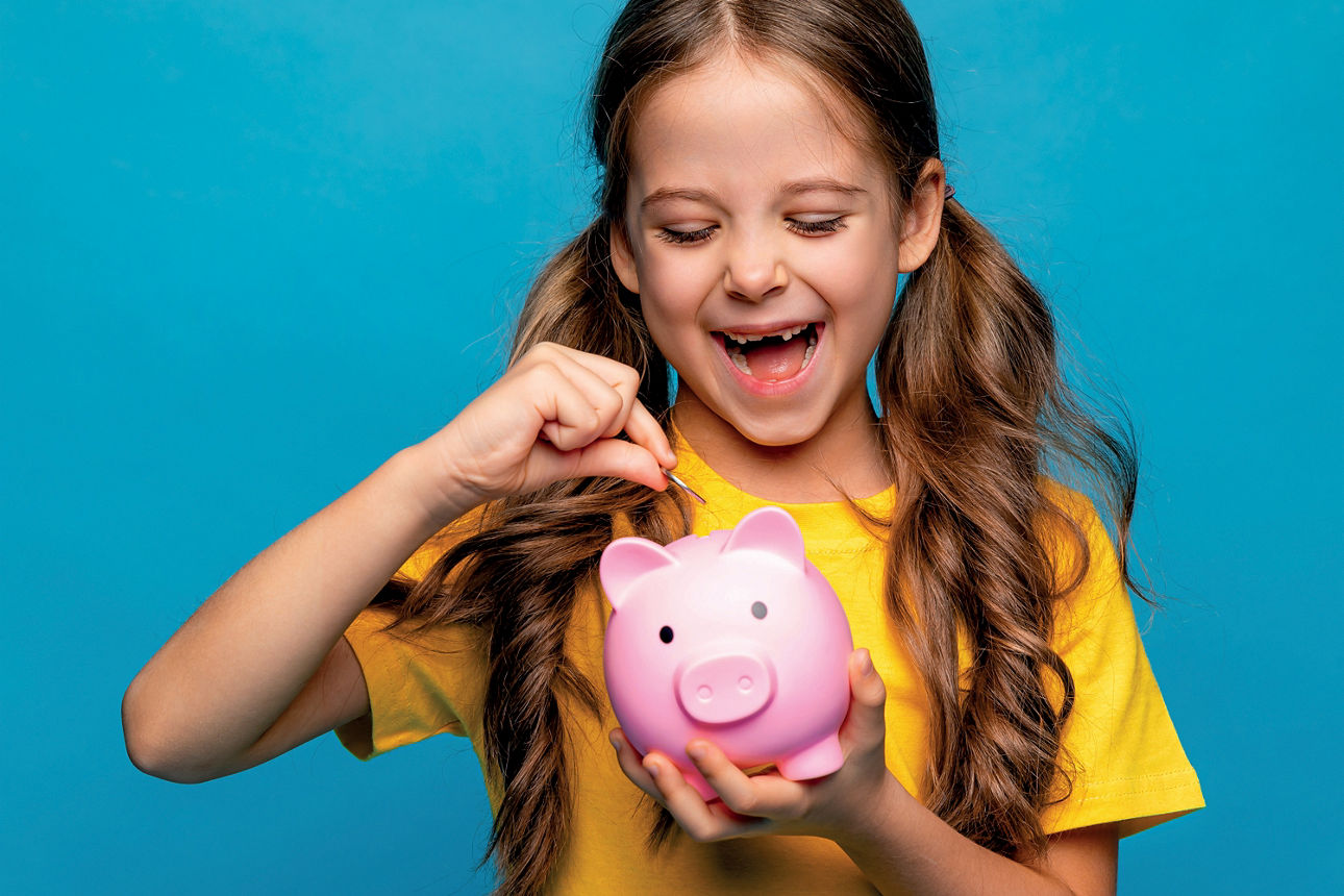 Mädchen in gelbem T-Shirt füllt Geld in ein Sparschwein
