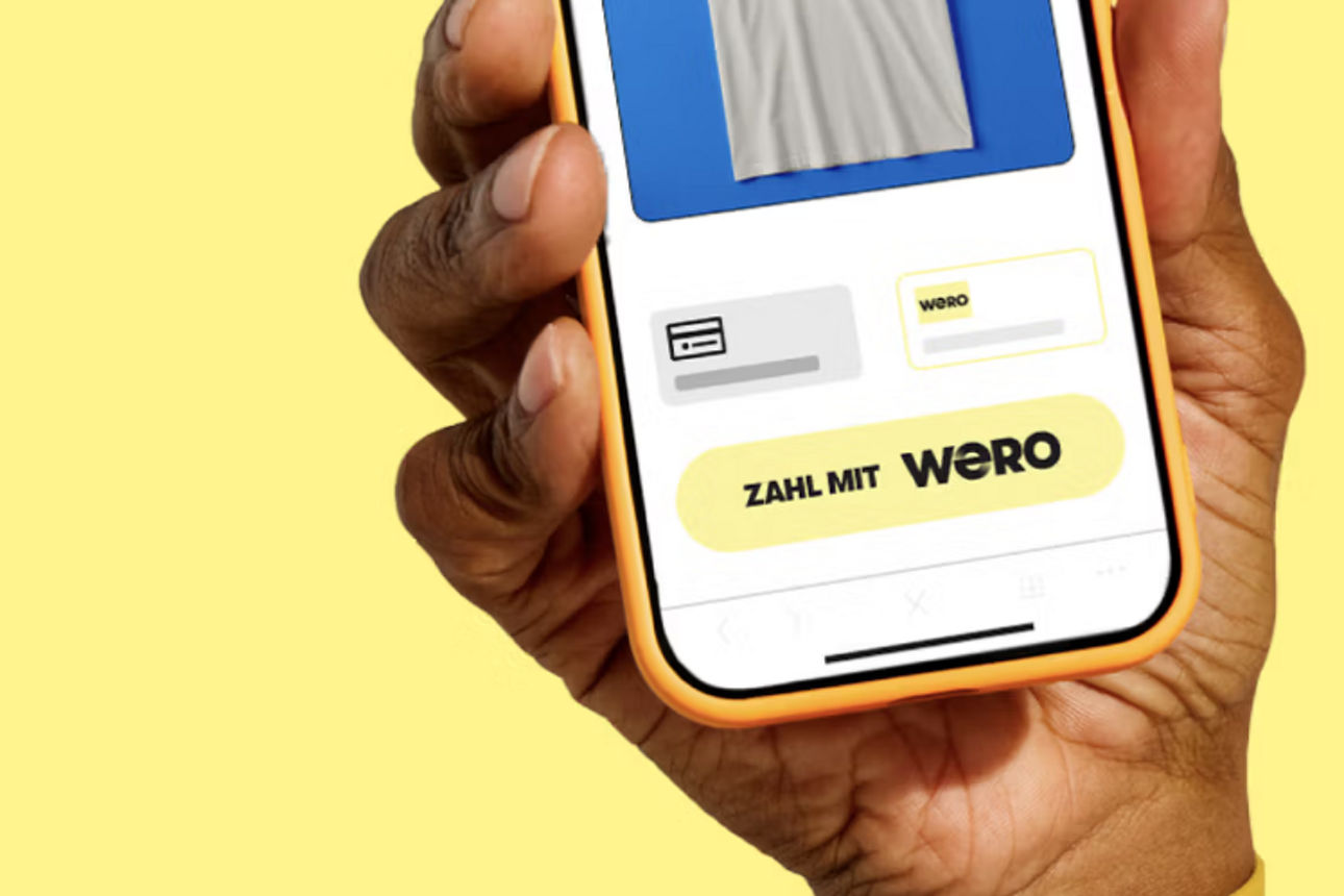 1 Hand mit Smartphones, auf der Anzeige sind Transaktionen mit Wero zu sehen.
