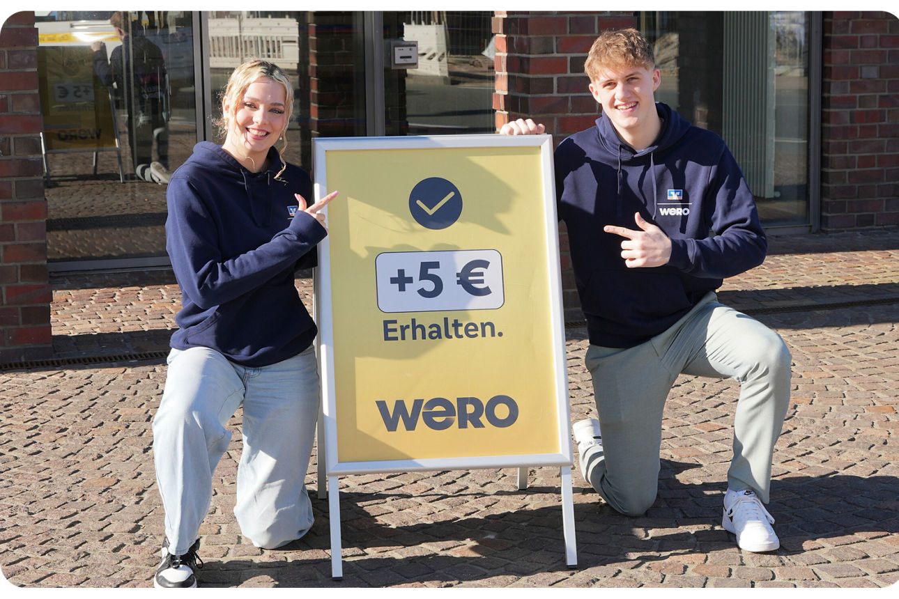 Frau und Mann stehen an einem Plakat mit der Aufschrift "Wero"