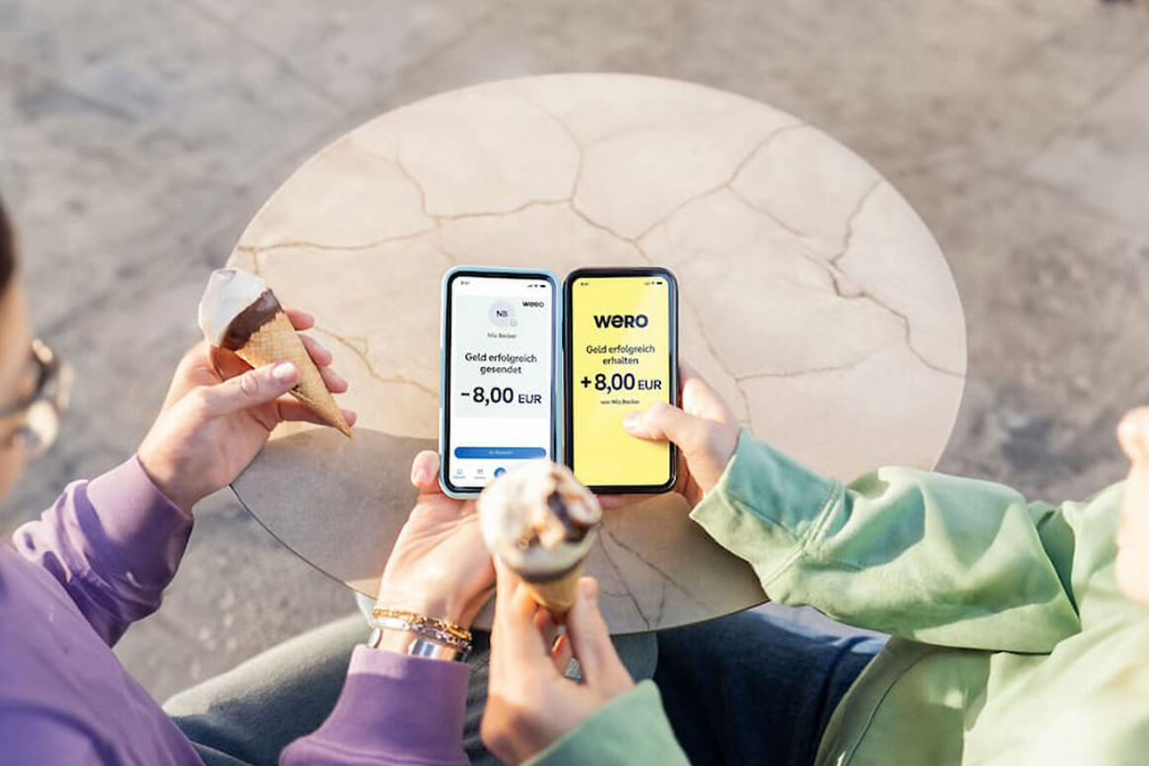 Zwei Eis-essende Personen nutzen ihre Smartphones für eine Wero Zahlung