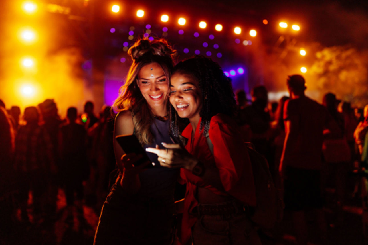 Zwei Frauen vor der Bühne eines Festivals mit einem Smartphone in der Hand