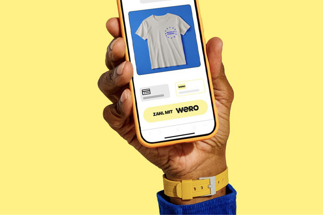 Eine Hand hält ein Smartphone hoch, auf dessen Screen sieht man Online-Shopping mit #VRNW_digitales_Bezahlverfahren