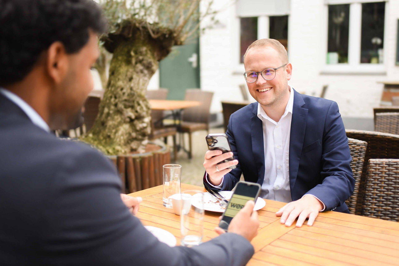 Zwei Männer sitzen mit dem Handy in der Hand im Außenbereich eines Restaurants.