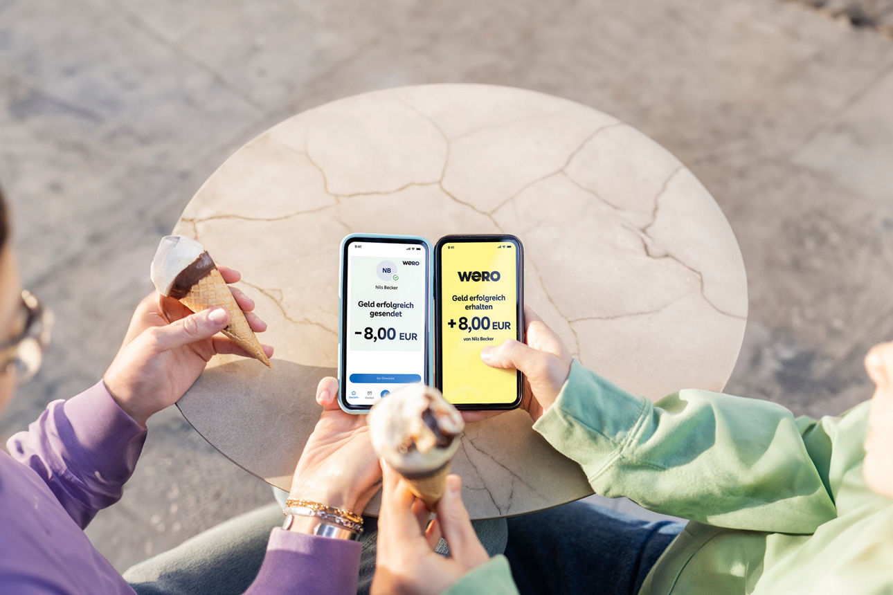 Zwei Damen halten ihre Smartphone beim Eissessen aneinander