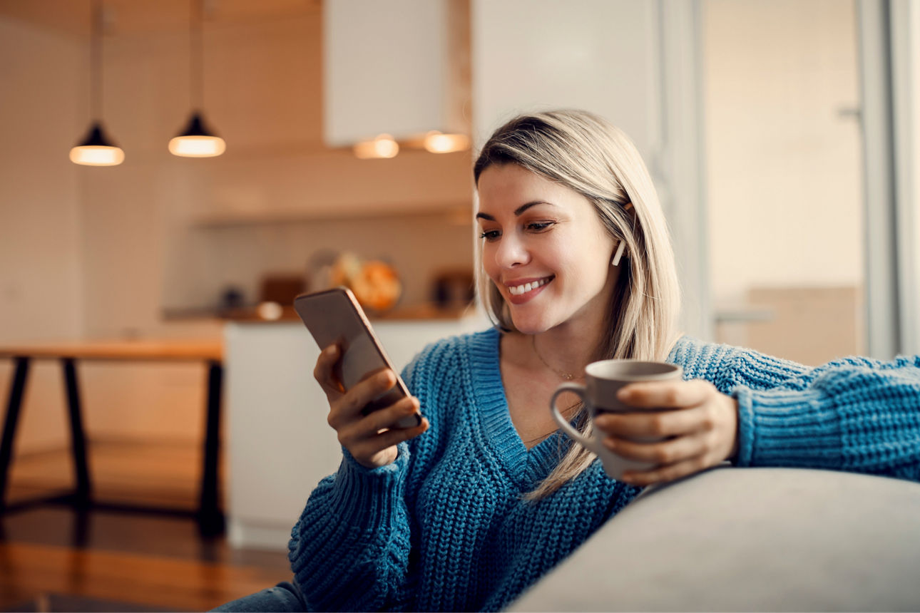 Frau mit Handy und Tasse in der Hand sitzt auf der Couch