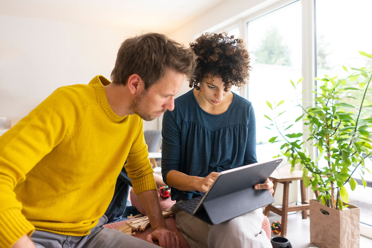 Ehepaar sitzt im Wohnzimmer und benutzt ein digitales Tablet