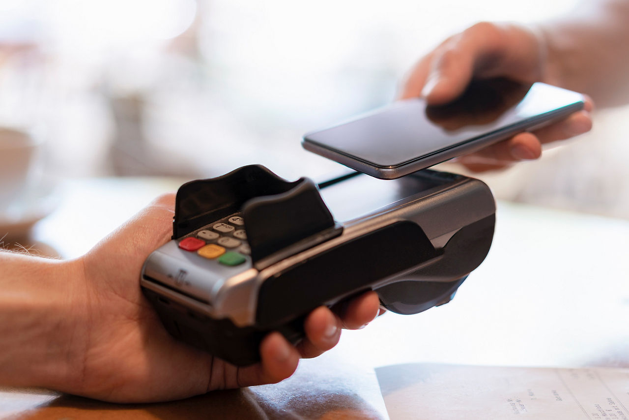 Ein Smartphone wird zum kontaktlosen Bezahlen an ein Kartenterminal gehalten