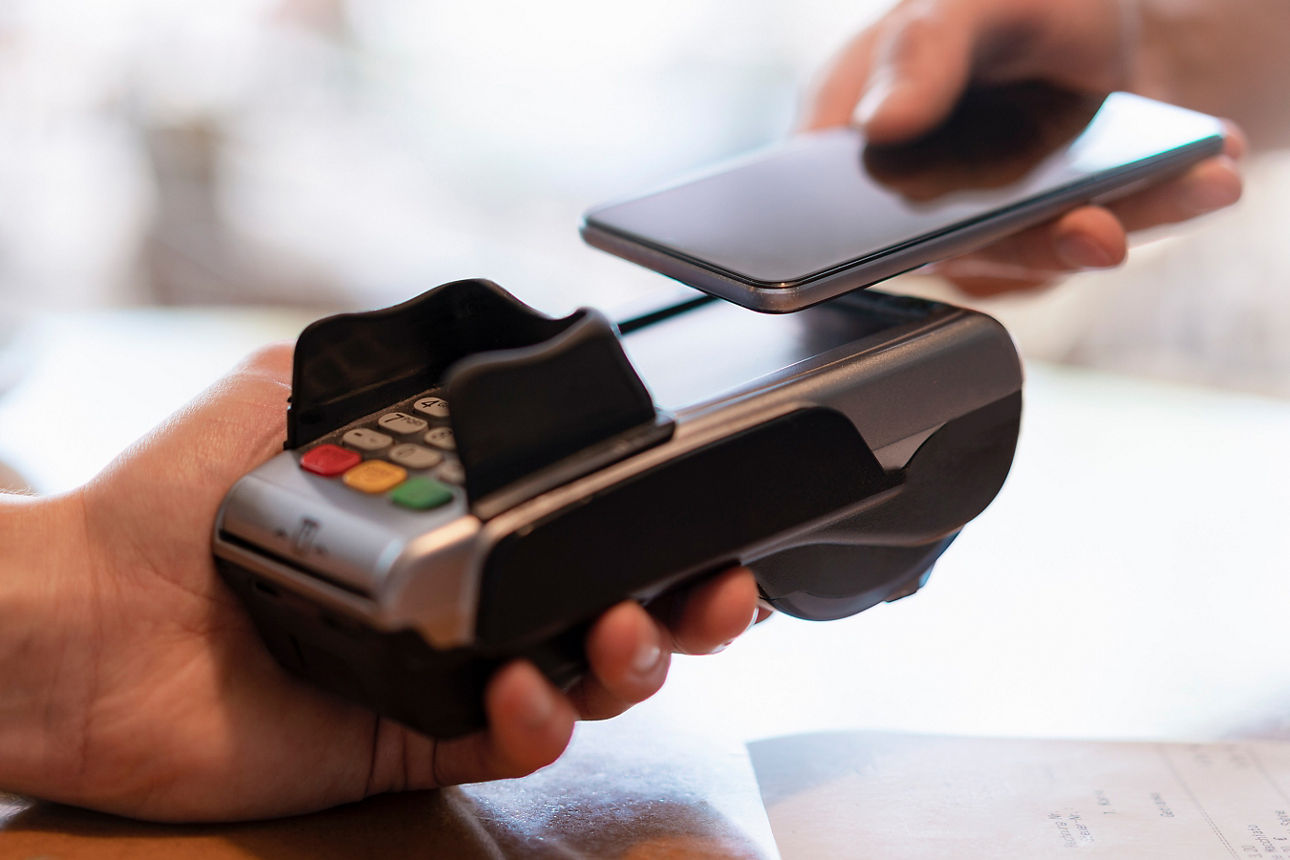 Ein Smartphone wird zum kontaktlosen Bezahlen an ein Kartenterminal gehalten