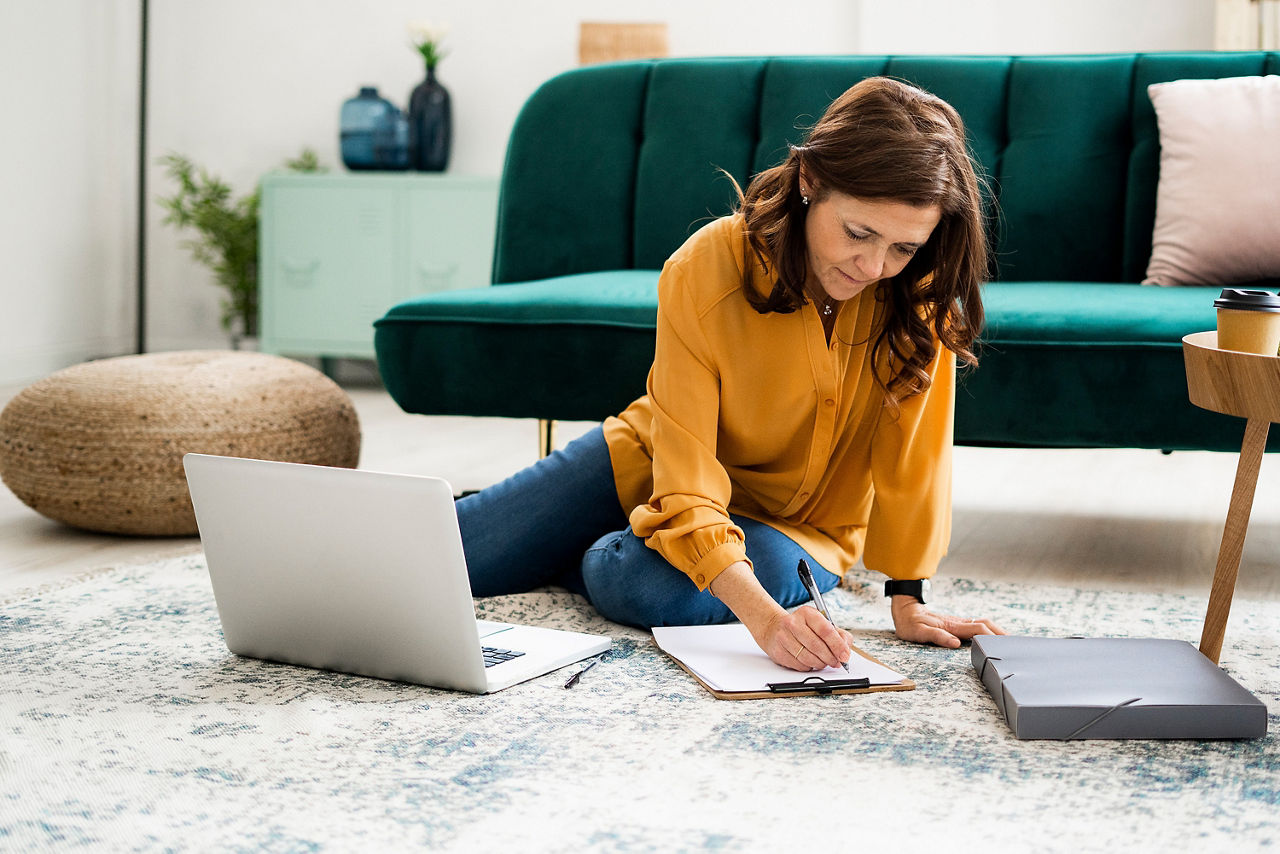 Eine Frau überweist Rechnungen am Laptop, während sie zu Hause auf dem Boden sitzt