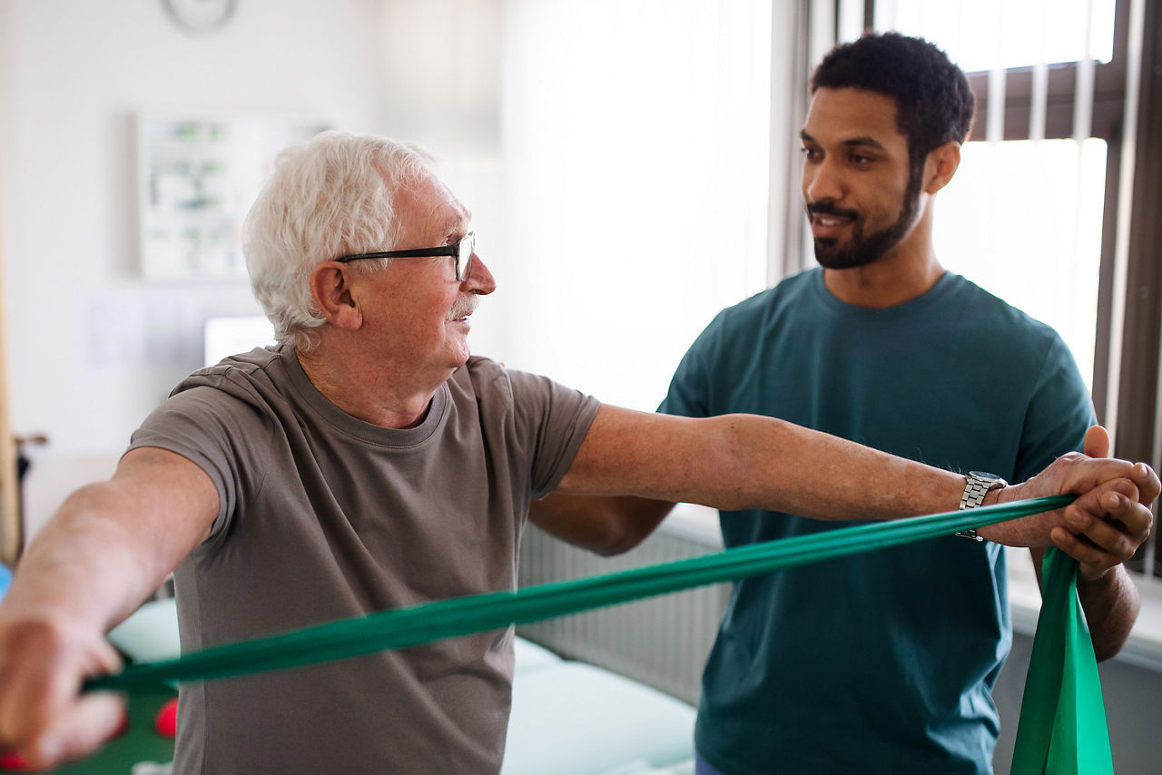 Physiotherapeut trainiert mit einem älteren Patienten in einem Behandlungsraum
