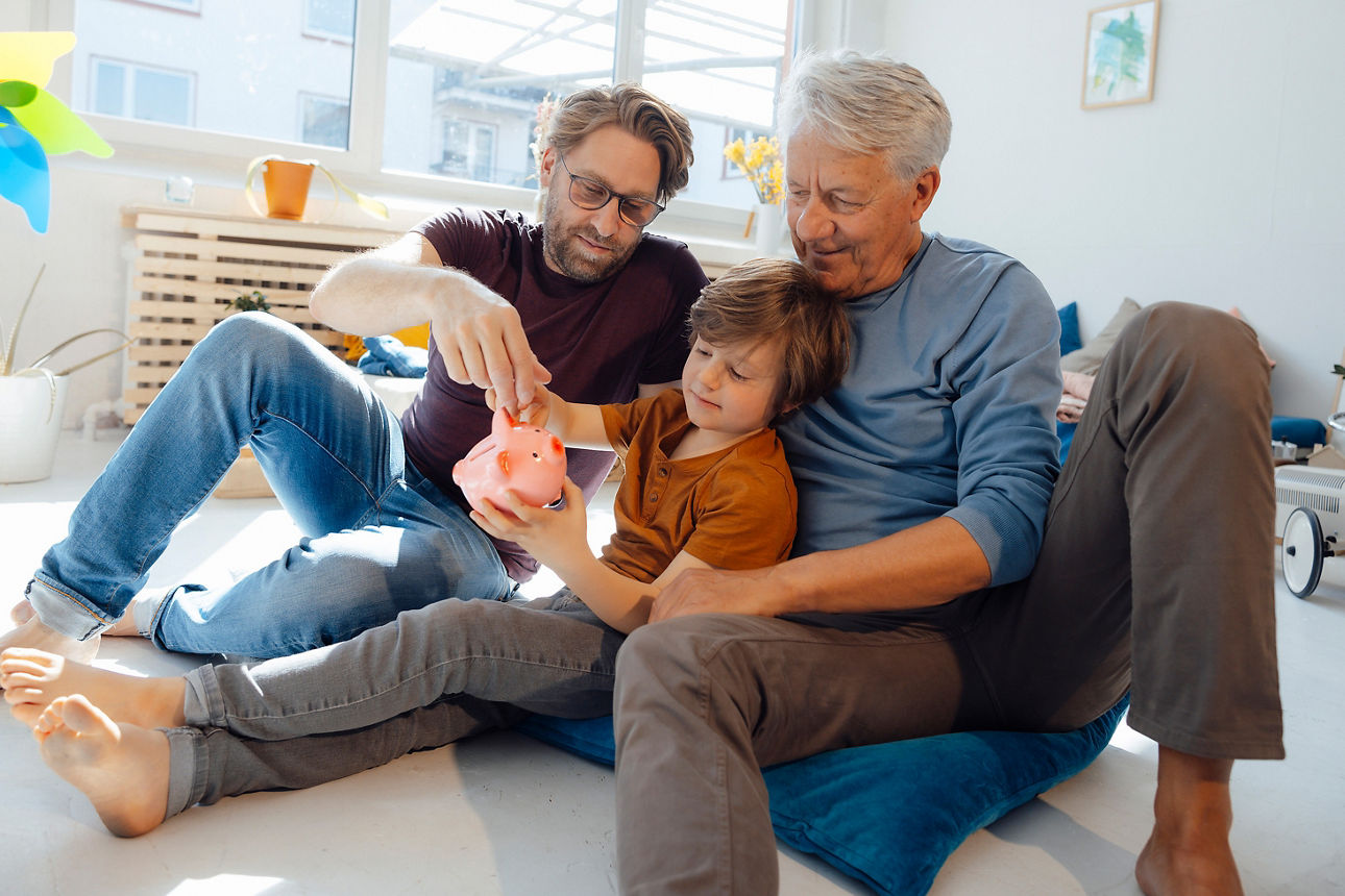 Älterer Mann mit Sohn und Enkel legt Geld in ein Sparschwein
