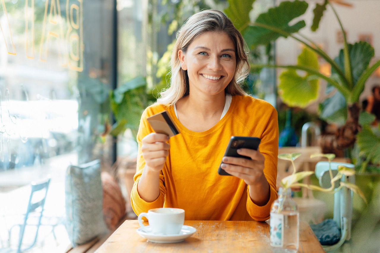 Glückliche Frau sitzt mit Kreditkarte und Smartphone in einem Café
