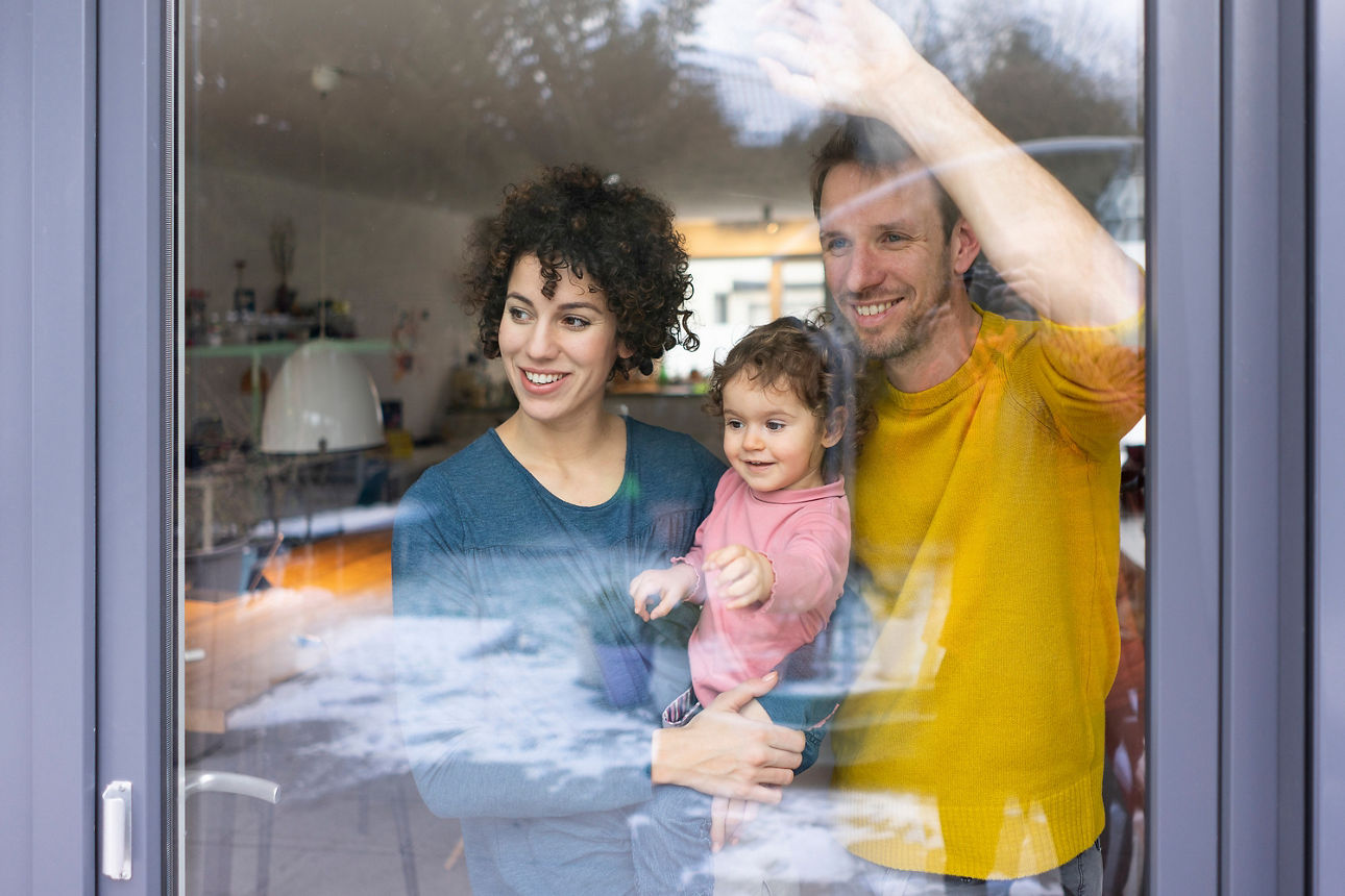 Glückliche Familie schaut aus dem Fenster, Mutter trägt Tochter