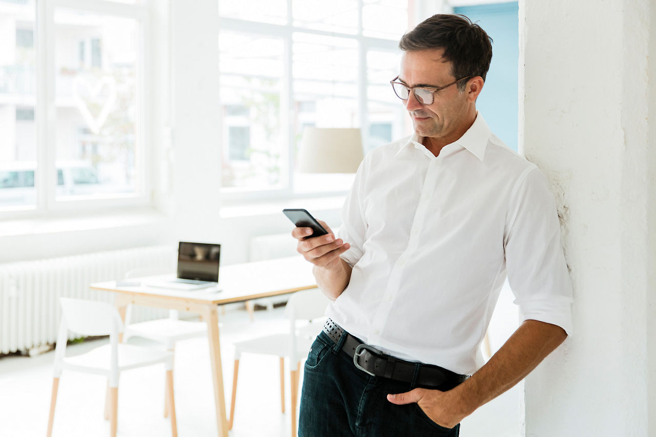 Geschäftsmann schaut auf sein Handy in hellem Büro