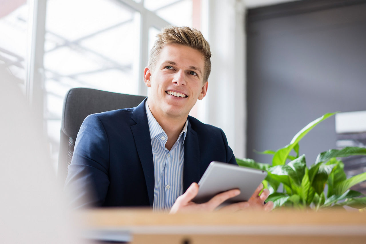 Mann sitzt am Schreibtisch und hat ein iPad in der Hand