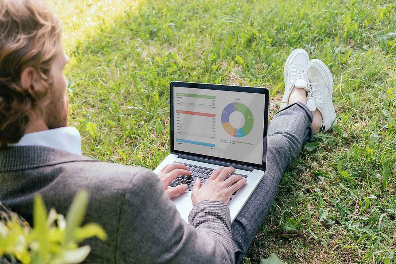 Mann sitzt auf einer Wiese mit aufgeklappten Laptop