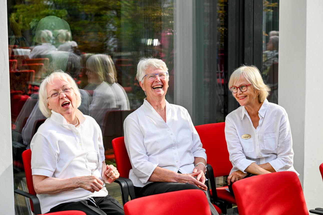 Drei Frauen sitzen auf roten Stühlen und lachen