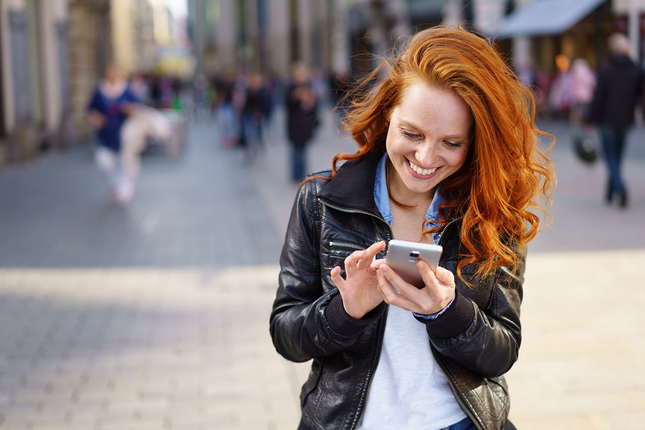 Eine Frau schaut lächelnd auf ihr Smartphone.