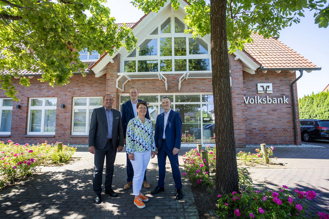 Das Team der Filiale Scharmede und ein Vorstandsmitglied der VerbundVolksbank OWL stehen vor der wiedereröffneten Filiale Sch