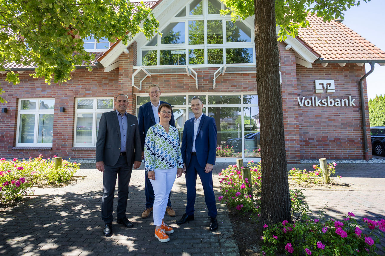 Das Team der Filiale Scharmede und ein Vorstandsmitglied der VerbundVolksbank OWL stehen vor der wiedereröffneten Filiale Sch