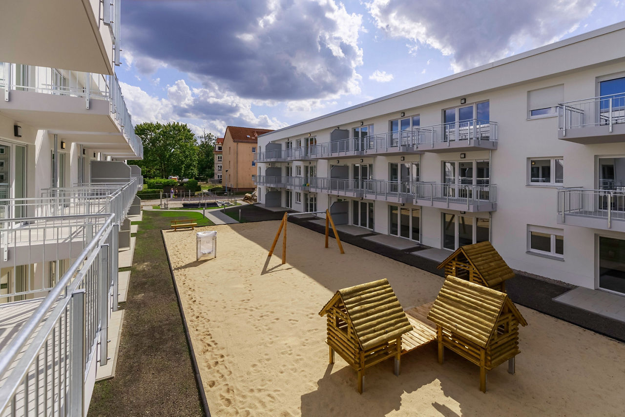 Außenaufnahme zweier Neubaugebäude mit Spielplatz dazwischen