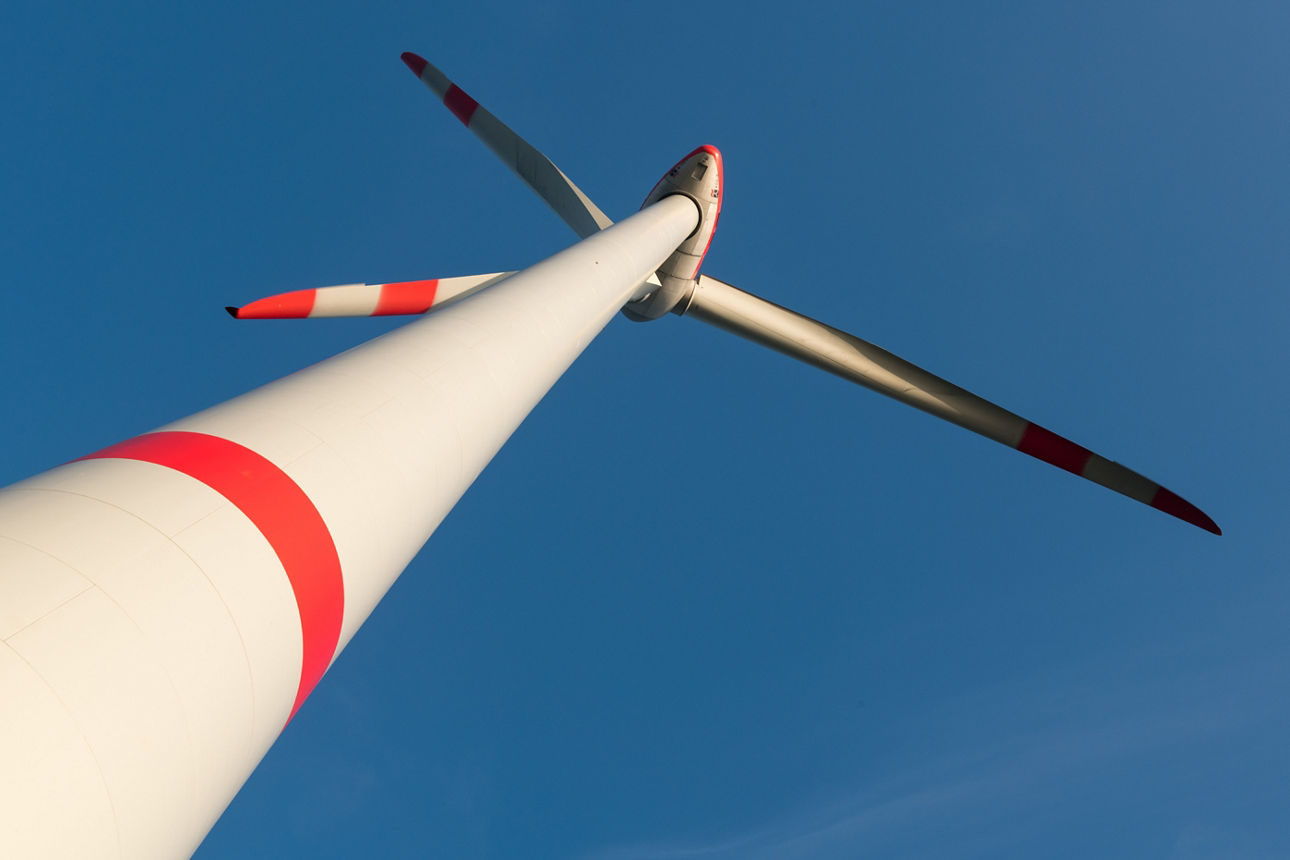 Nahaufnahme einer modernen Windkraftanlage mit rot-weiß-markierten Rotorblättern, vor einem klaren, blauen Himmel .